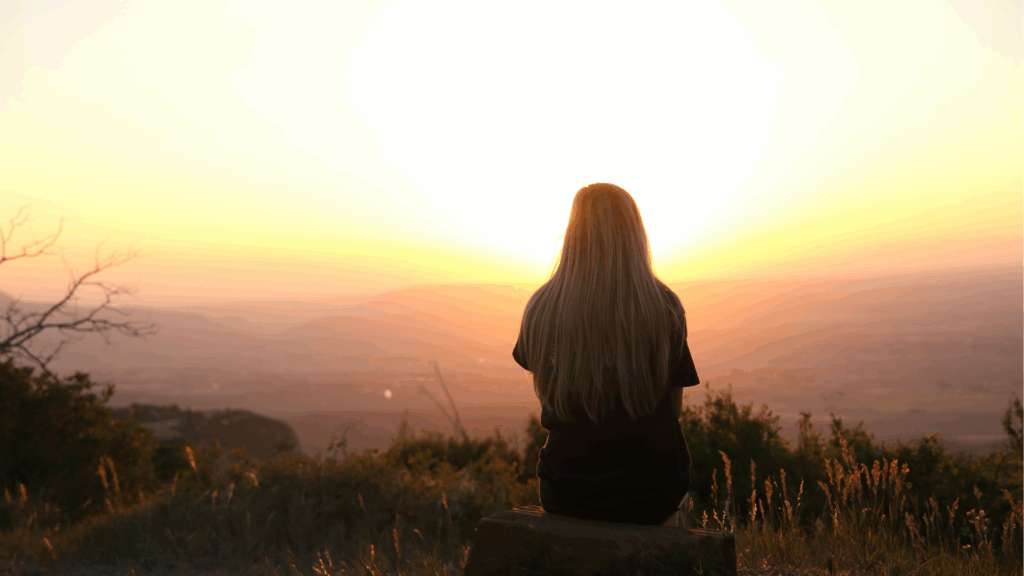 mujer en lo alto de la montaña oteando el horizonte en un atardecer